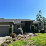 Suburban home with a neatly trimmed lawn and various shrubs, showcasing a welcoming entrance with stone pillars and a garage.