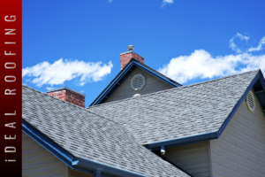 Residential asphalt shingle roof with brick chimneys and blue trim under a clear blue sky, showcasing durable roofing materials