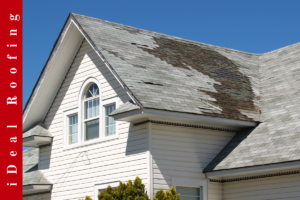 A house with a damaged, weathered roof and missing shingles against a clear blue sky. The siding is white. The text "iDeal Roofing" is on a red vertical banner.