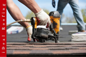 Worker using a yellow nail gun on shingles under a blue sky, highlighting professional workmanship in roof repair vs roof replacement projects.