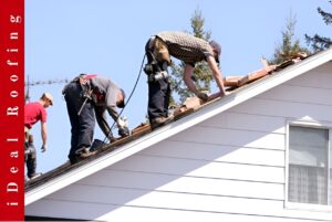 Three workers in safety gear carry out emergency roof repair on a sunny day, working efficiently with tools and materials while trees fill the background.