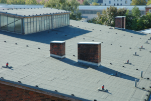 Close-up of a flat bitumen rooftop with chimneys; poor drainage often shortens a commercial roof's life.