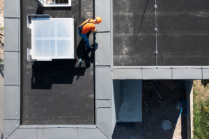 Overhead view of a worker inspecting a flat membrane; lack of maintenance shortens a commercial roof's life.
