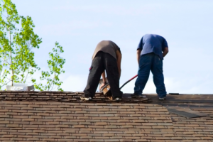 Two roofers repairing a shingle roof, emphasizing why professional roof inspection tips save money on repairs.
