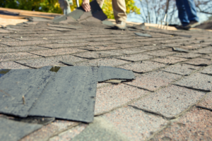 Close-up of damaged, curling, and lifting asphalt roof shingles being removed during a repair.