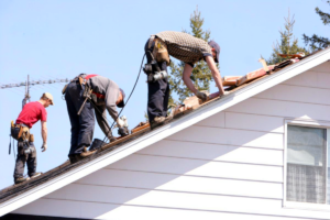 Three roofing contractors wearing safety gear while installing new shingles on a residential roof.