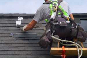 A roofer inspecting shingles near a gutter system, emphasizing roofing warranties explained.