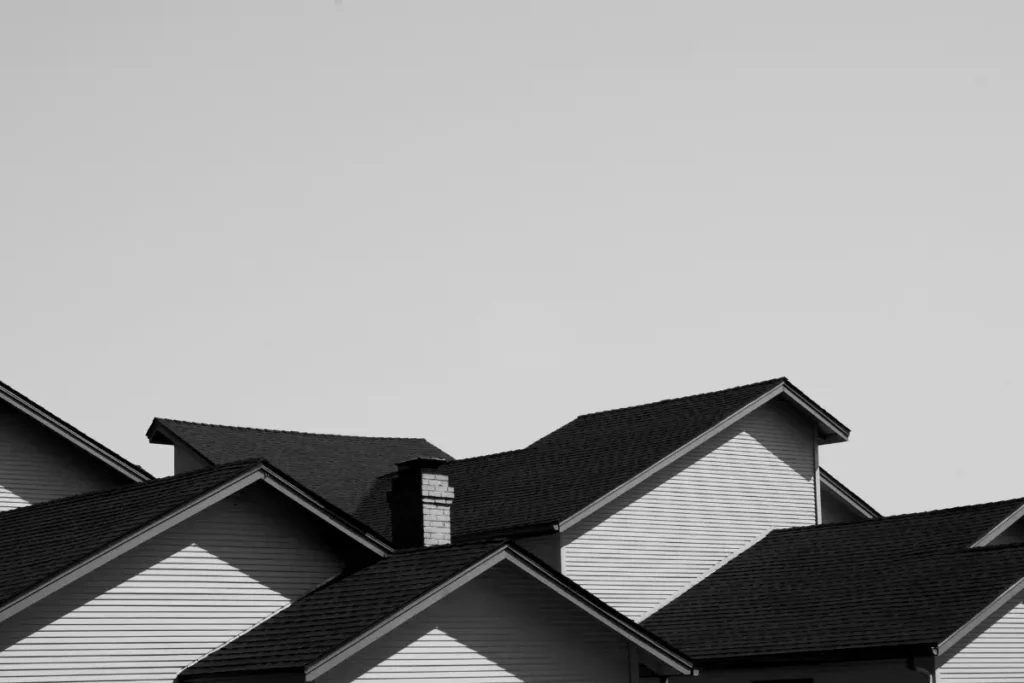 A black and white photograph showcasing a complex residential roofline with multiple overlapping gables and dark asphalt shingles, highlighting durable roof installation and workmanship.