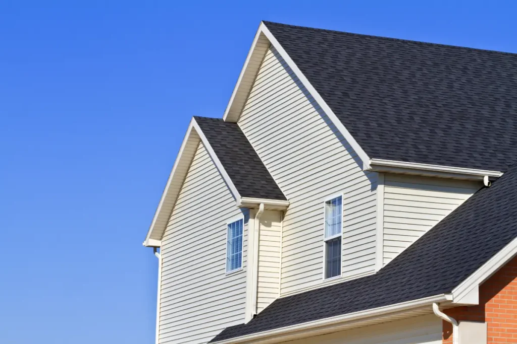 Exterior view of a two-story residential home with clean dark grey asphalt shingle roofing, light beige siding, and white gutters.