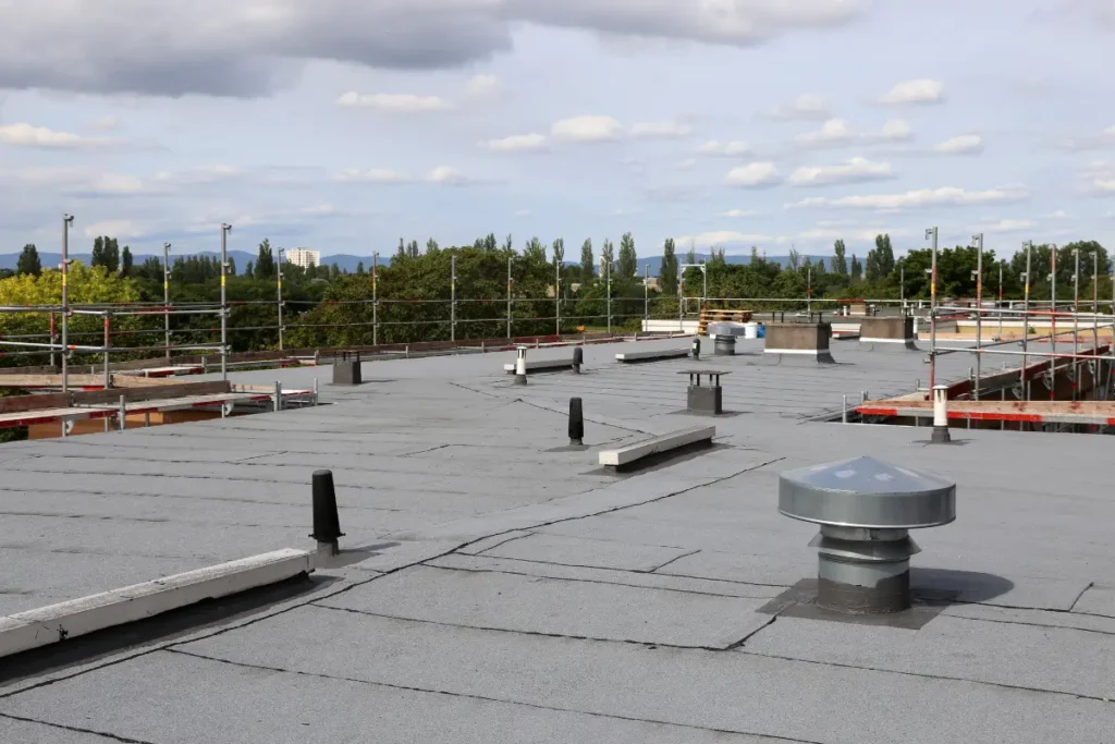 Rooftop view of a commercial flat membrane roof with multiple vent pipes and scaffolding surrounding the edges