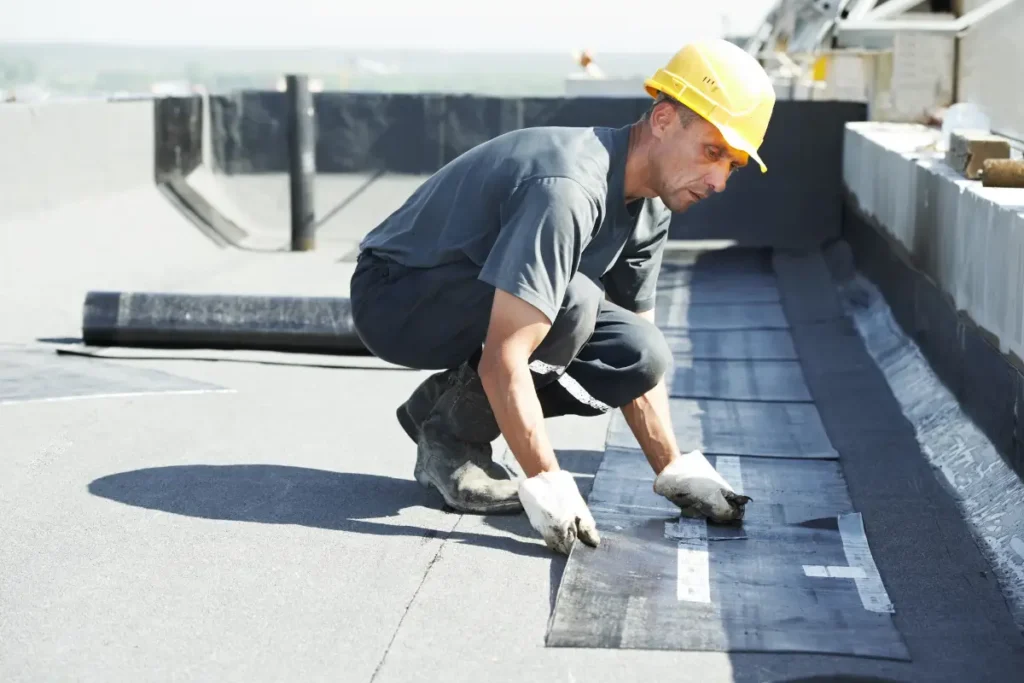 Construction worker in a hard hat laying down membrane roofing material on a flat commercial roof