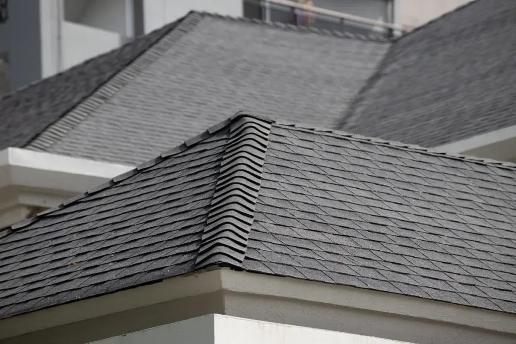 Dark grey asphalt shingles and ridge cap detailing on a multi-sloped residential roof.
