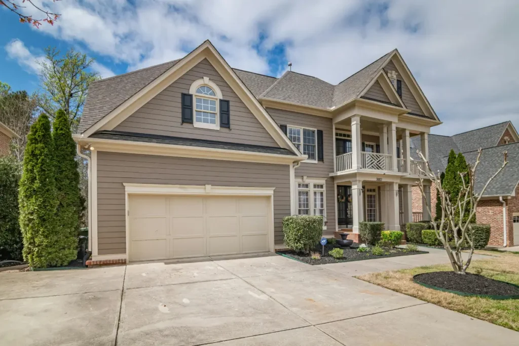 Two-story suburban house featuring taupe siding, a multi-gabled architectural shingle roof, and a two-car garage under a partly cloudy sky.