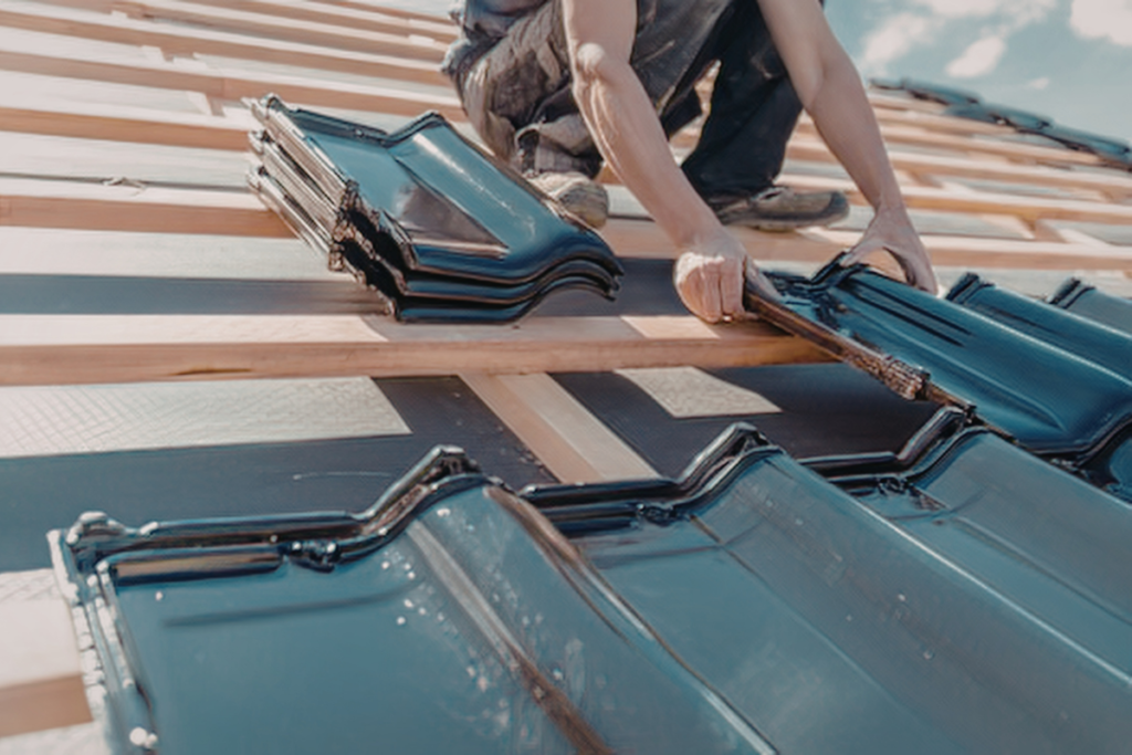 Roofer installing dark glazed roof tiles onto wooden battens during a commercial roofing project.