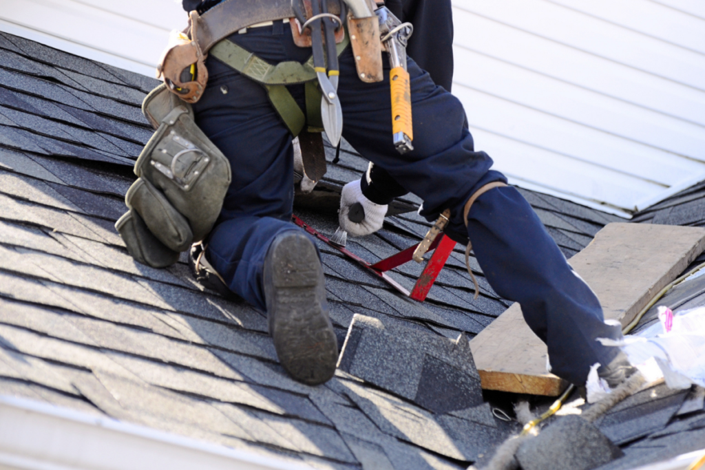 Worried homeowner holding a metal bucket to catch water pouring from a leaking ceiling while calling for emergency roofing repair.