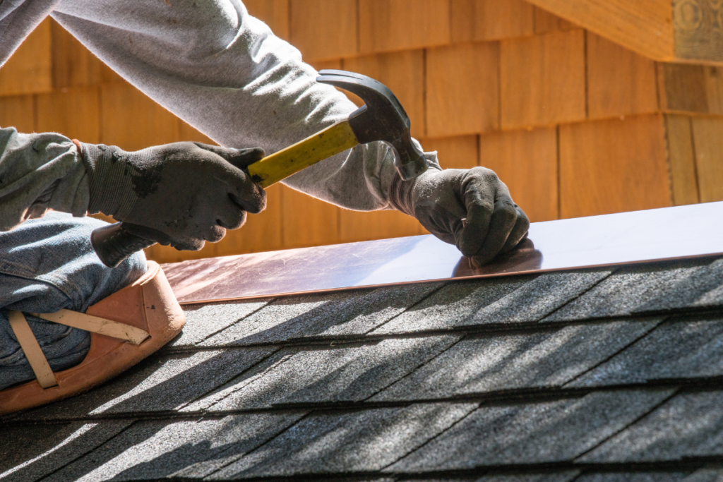 Professional roofer using a claw hammer to secure copper flashing along the roof edge during final installation and inspection.
